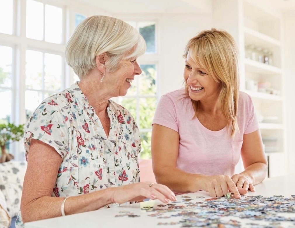 A companion sharing a warm, joyful moment with an elderly person living with dementia at home